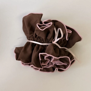 Macro view of coffee brown plaid scrunchie with pink wavy edges and satin bow detail