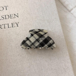 Macro side view of a black and white checkered acetate hair claw clip on a fabric book