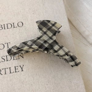 Detailed close-up of a checkered acetic acid hair claw clip on a soft textured fabric surface