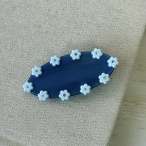 Pince à cheveux florale bleu marine avec mini strass sur un fond beige texturé