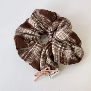 Detailaufnahme von braunem Karo-Haargummi mit Lederschleife, Knopf und Happiness-Label