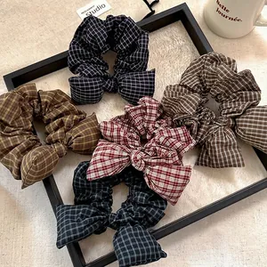 Five assorted plaid pattern bow hair scrunchies displayed on a beige textured background