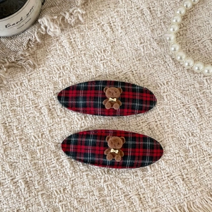 Detail view of two red plaid hair clips with cute flocked brown bear decorations
