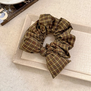 Elegant brown plaid scrunchie with a bow tie design on a beige tray for women hair styling