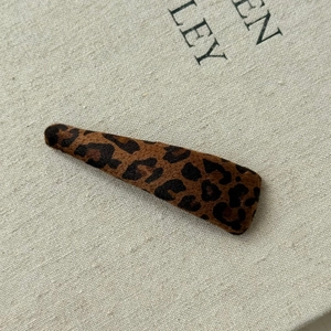 Vintage leopard print hair clip with soft flocking texture on a minimalist beige background