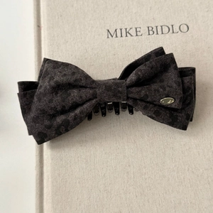 Detailed view of a leopard print bow hair clip with a gold logo on a vintage book