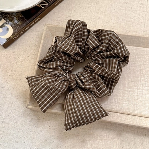 Detail view of brown plaid bow scrunchie made of premium fabric on a beige textured tray