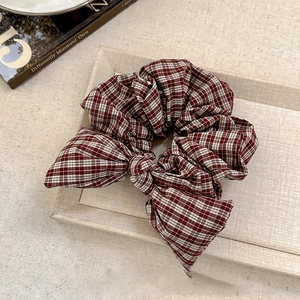 Macro shot of minimalist red brown plaid bow scrunchie on a textured tray