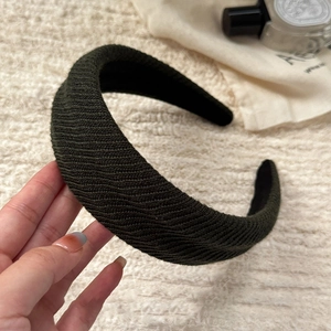 Detailed close-up of dark green thick knitted headband with textured wave pattern