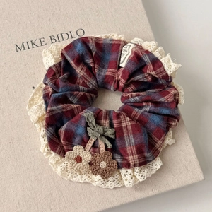 Detail eines roten Karo-Scrunchies mit Spitzenrand und gestrickter Gänseblümchen-Deko