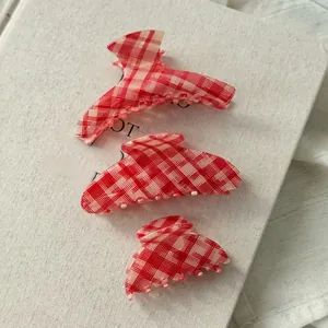 Three sizes of red and white gingham hair claws displayed on a vintage book with lace