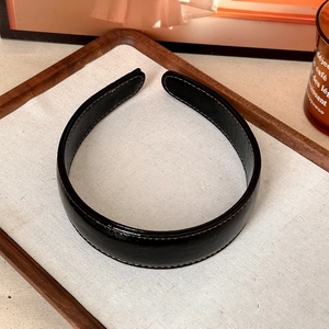 Detail of black faux leather headband showing fine stitching and polished texture finish