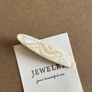 Detail of acetate marble hair clip featuring FRANCE Handmade lettering on off-white texture