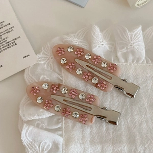 Dettaglio di fermagli per capelli in acetato rosa con strass floreali su pizzo bianco