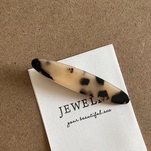 Detailed close-up of cream and black tortoiseshell acetate hair clip with gold text