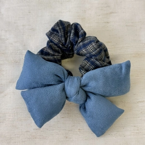 Detail eines blauen Wildleder-Bogens und Karo-Haargummis auf elegantem weißem Stoff