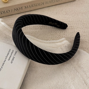 Close-up of black striped fabric headband with gold logo on soft knitted background