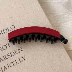 Dettaglio del fermaglio a banana in acetato rosso opaco con denti neri su un libro