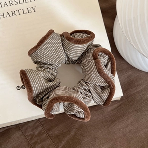 Close-up of brown striped scrunchie with plush trim on a minimalist book background
