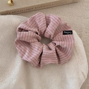 Close-up of a striped hair scrunchie with a logo label on soft beige knit fabric