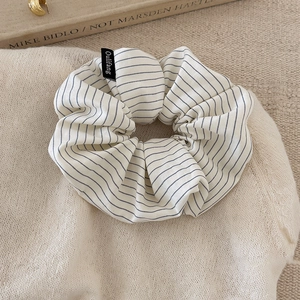 Close-up of a striped fabric scrunchie with brand label on a soft knit background