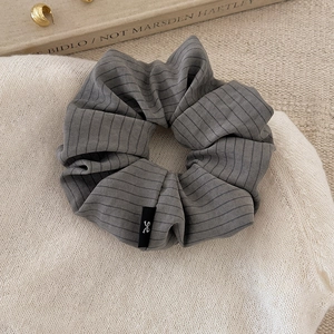 Detailed view of grey striped fabric scrunchie with subtle ribbon bow tag detail