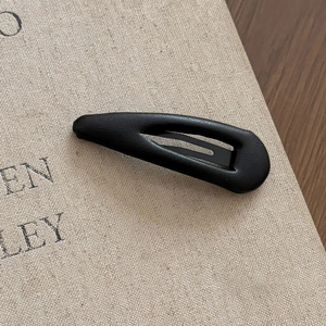 Macro shot of a black faux leather teardrop BB hair clip on a textured book surface