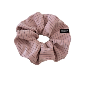 Pink striped fabric scrunchie with soft elastic and black woven brand label on white background