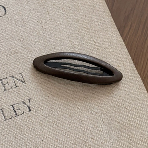 Detailed close-up of dark brown leather oval hair clip with textured litchi grain finish