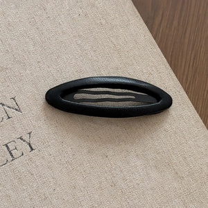 Close-up of matte black leather textured oval hair clip on a minimalist canvas background