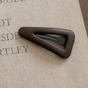Macro shot of dark brown leather texture and triangular metal hair clip design