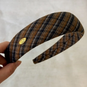 Detail eines Vintage Karo-Haargummis in Blau-Braun mit graviertem goldenen Metallemblem