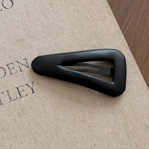 Detailed close-up of a minimalist black leather triangle hair clip on textured background