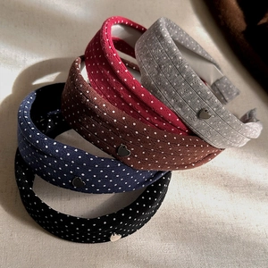 Five assorted polka dot fabric headbands with silver heart charm on textured background