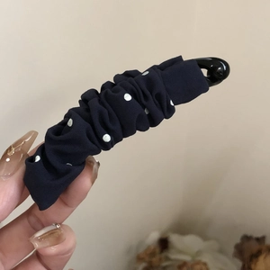 Handheld view of a stylish black polka dot pleated fabric banana hair clip for women