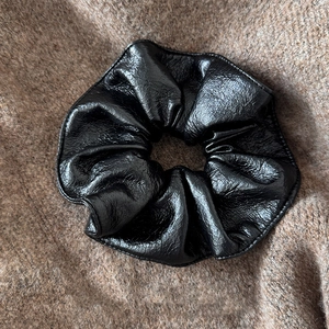 Gros plan du chouchou en cuir PU noir avec texture plissée sur tissu en maille