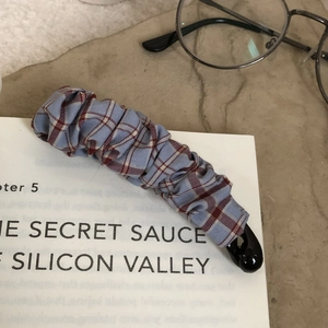 Detailed view of a blue and red plaid fabric banana hair clip on a book background