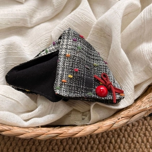 Detail of tweed triangle hair claw clip with colorful dots and a red bow on white fabric