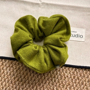 Detail of green knitted plush scrunchie showing soft texture and woven label on fabric