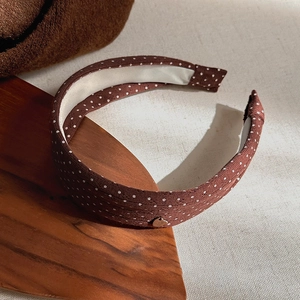 Close-up of brown polka dot knitted headband with heart charm on a wooden tray