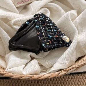 Detail of tweed and leather triangle clip with large pearl and gold logo charm