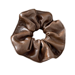 Chouchou en cuir marron foncé avec coutures détaillées et texture vintage sur fond blanc
