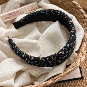 Close-up of black tweed headband with colorful threads and sequins on linen background