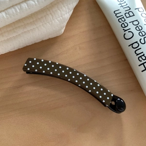 Close-up of a brown polka dot banana hair clip on a minimalist wooden surface