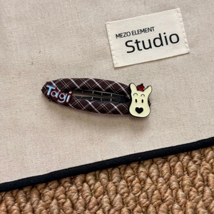 Makroaufnahme der braun karierten BB-Haarklammer mit Tagi-Logo und Cartoon-Bär-Detail