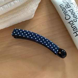 Detail of navy blue polka dot banana clip on light wood background showing glossy finish