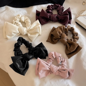 Five assorted PU leather bow scrunchies in cream, red, and brown on white fabric