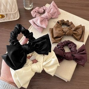 Five assorted colors of leather bow hair scrunchies displayed on a wooden surface