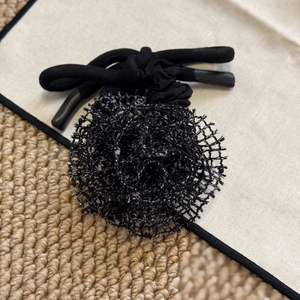 Détail d'un chouchou rose en maille noire avec pétales superposés et bande tubulaire nouée