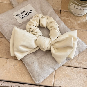 Detailed view of cream leather bow scrunchie with fine texture on a beige canvas bag